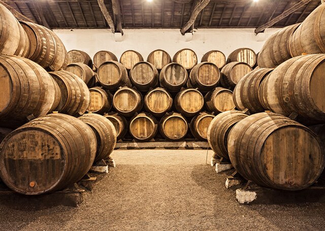 Photograph of a cellar containing stacks of unpainted wooden barrels.