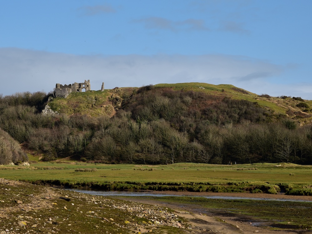 A ruined castle silhoutted on a hill overlooking a river valley.