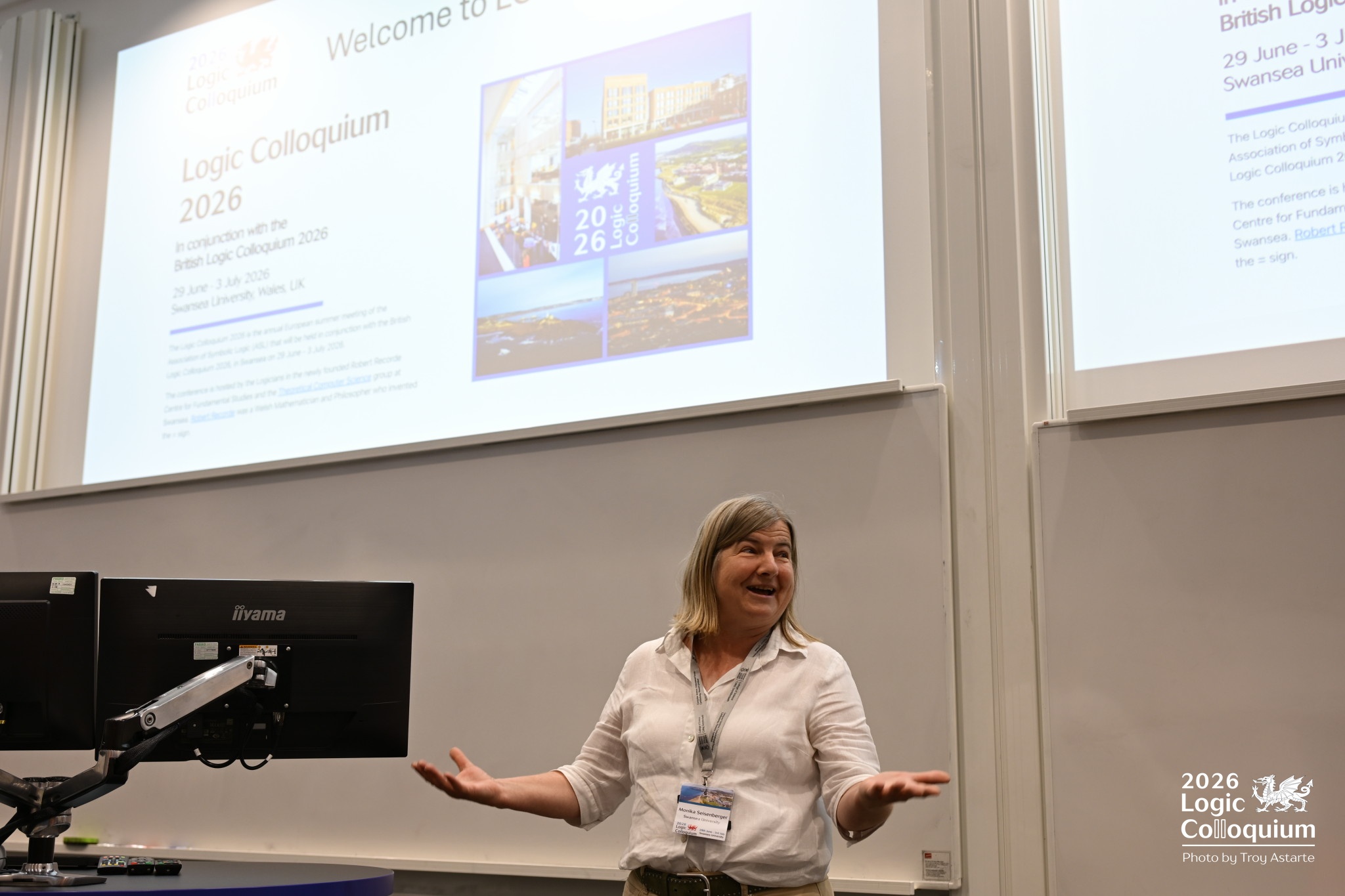 Photograph of a welcoming academic with arms spread wide in a lecture theatre.