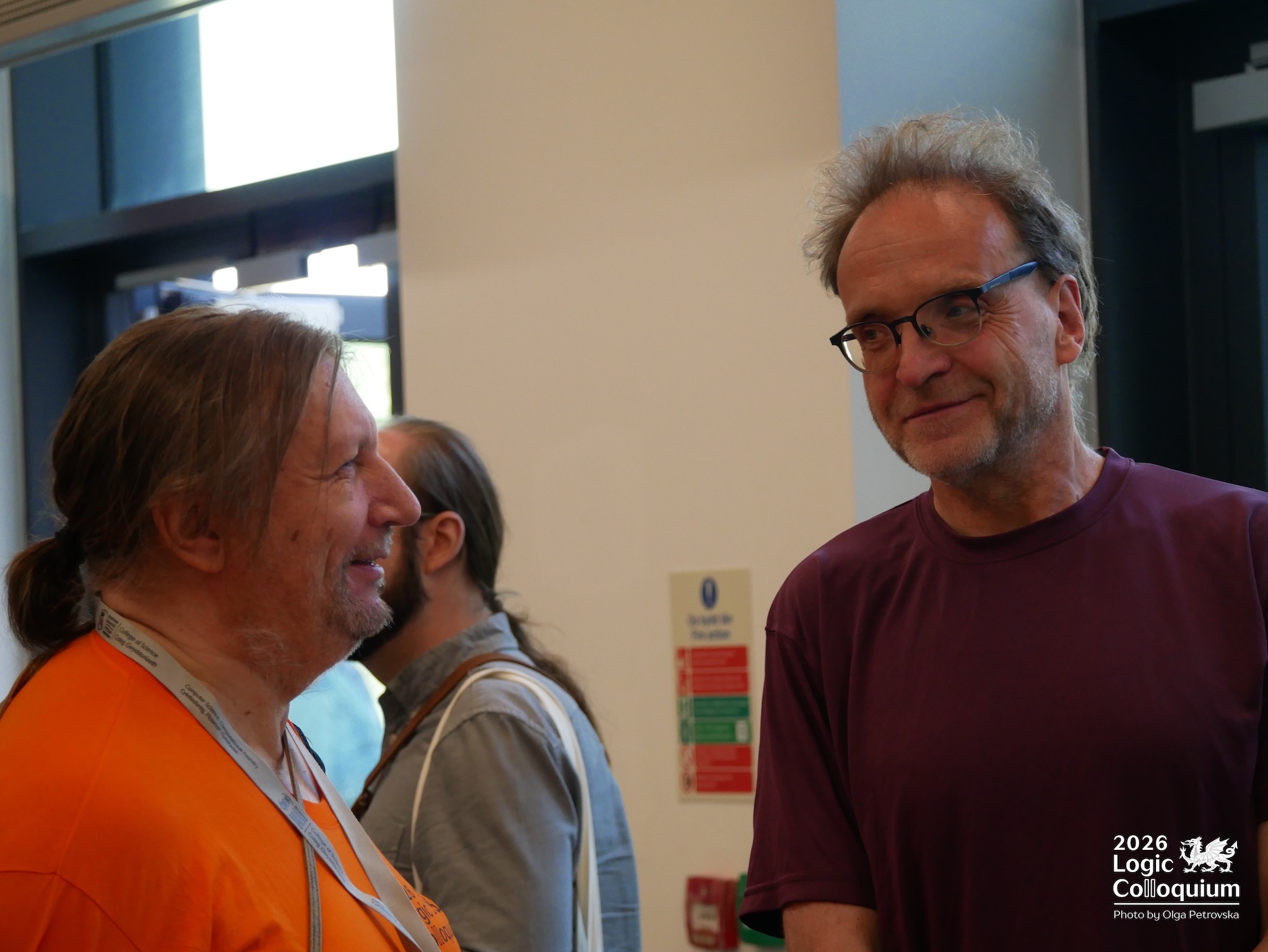 Photograph of two people smiling, perhaps wryly, at each other. One wears an orange T-shirt.