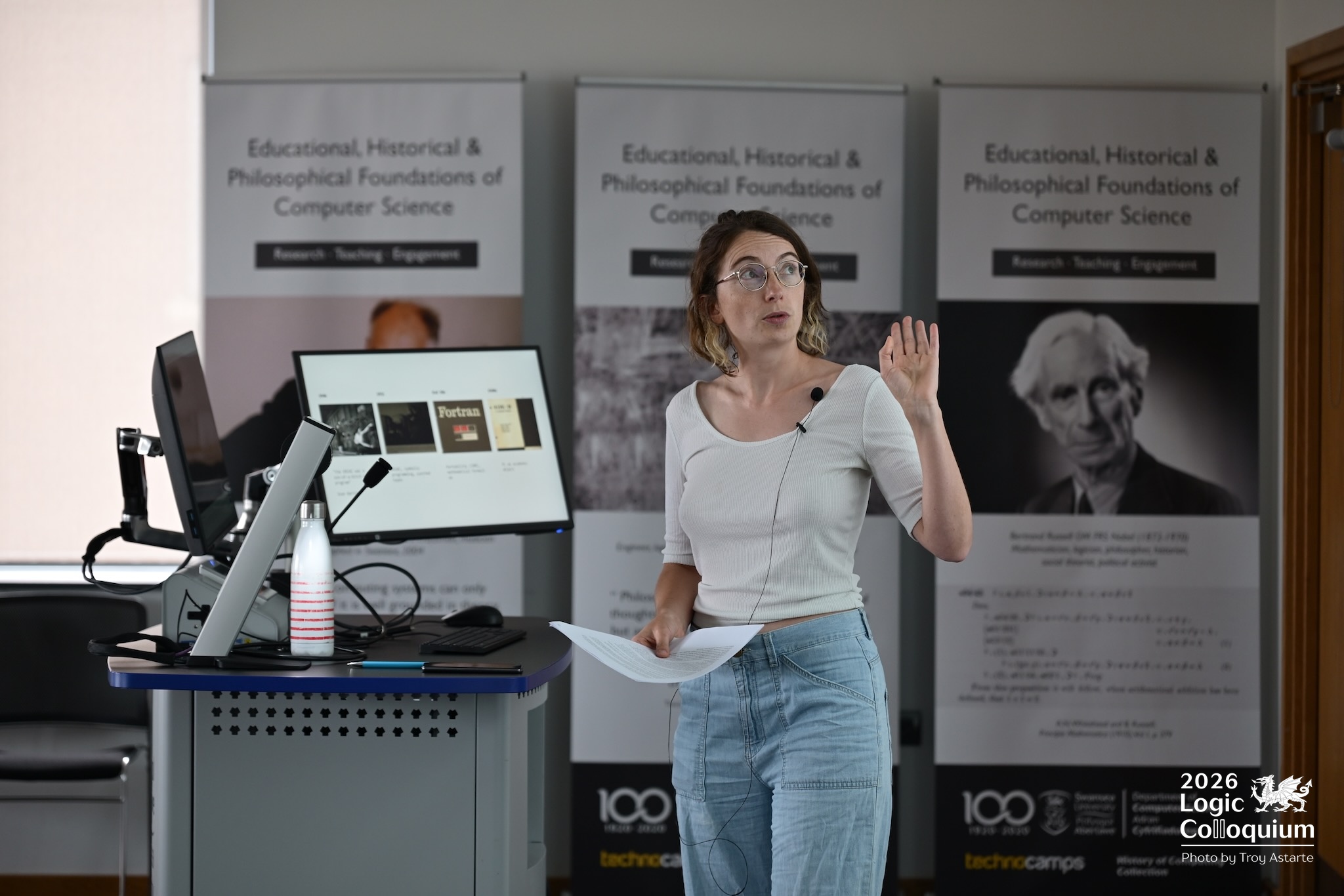 Photograph of an academic talking while Bertrand Russell watches inscrutably.