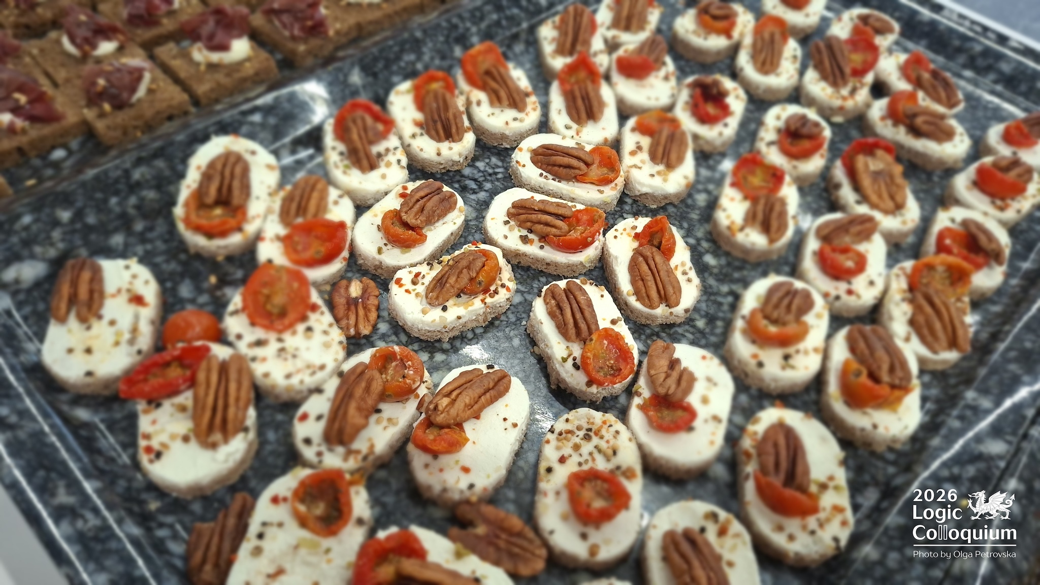 Photograph of a tray of ovals of something like chees with a chilli slide and pecan nut.