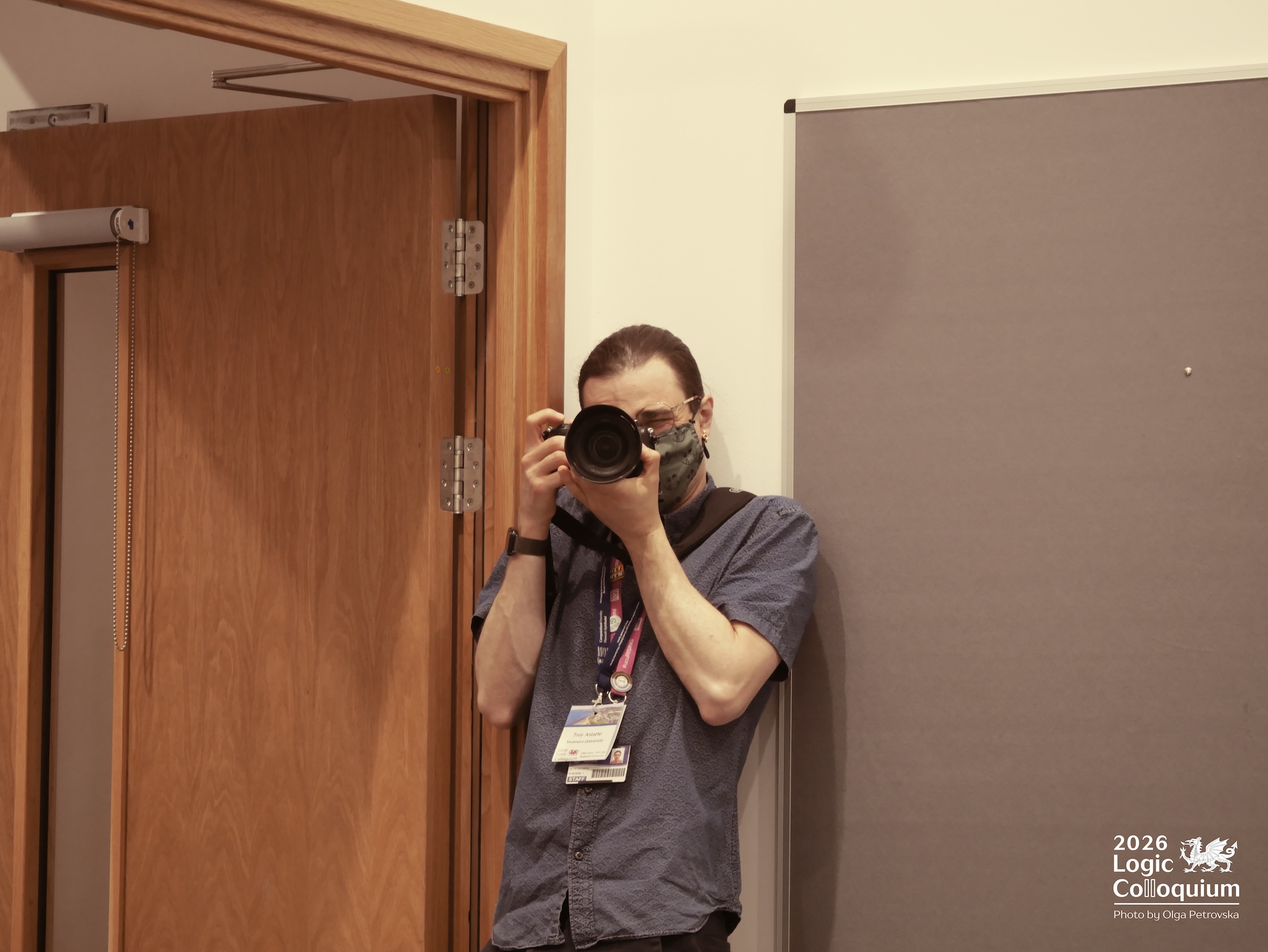Photograph of ... oh, it's me! Troy! A person in a blue shirt holds a camera obscuring most of their face while Olga takes a photo of them.