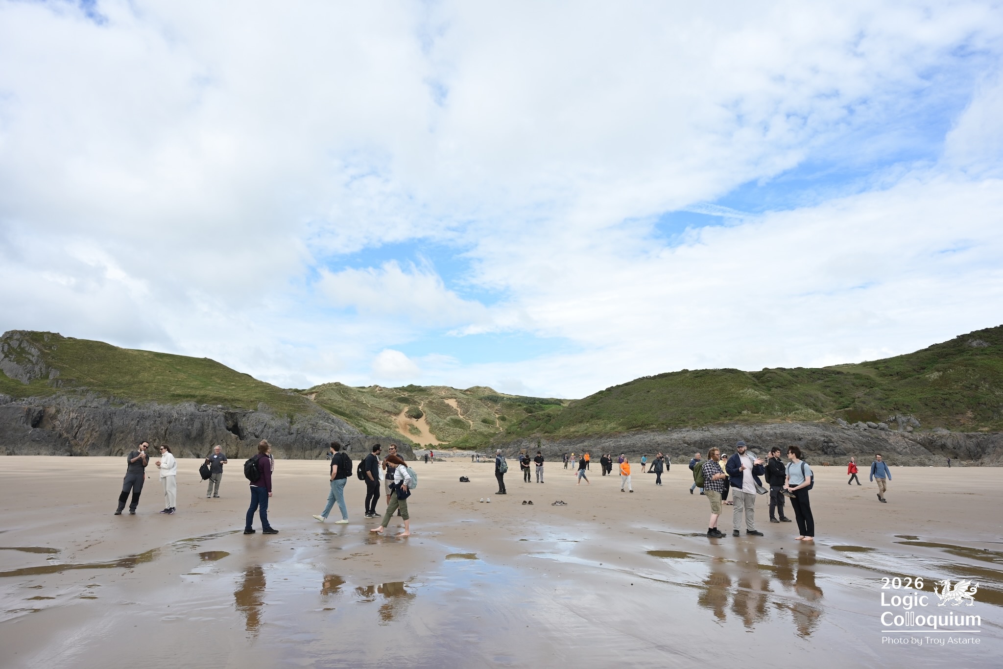 Photograph of logicians milling about on a beach at the edge of the water. The photographer's feet were probably wet.