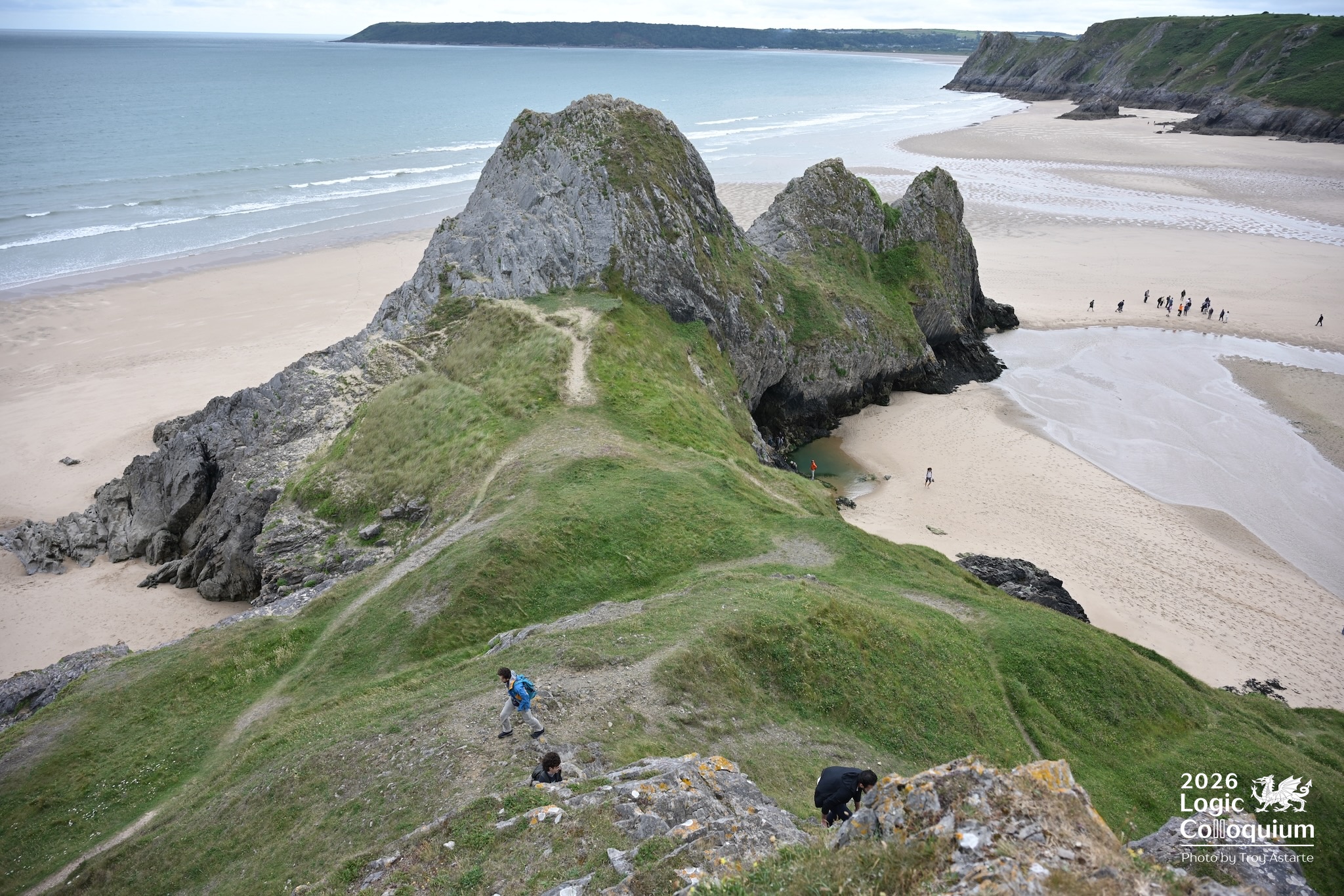 photograph of a few adventurous conference-goers climbing some cliffs, with the sweep of the bay behind, and a larger group of more cautious attendees standing in the far distance.