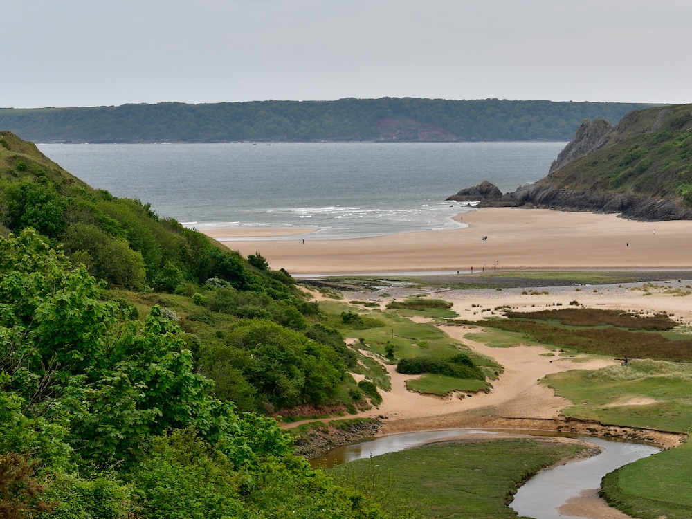 Photograph of a river valley opening onto a beach with lush green vegetation on the side.