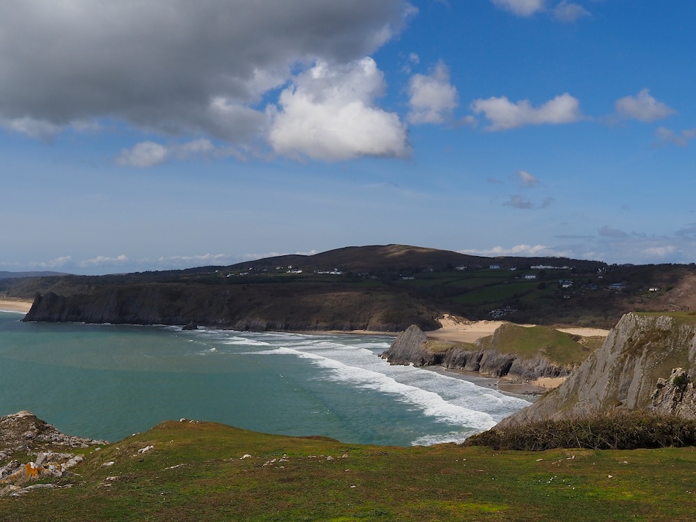 Photograph of three pointed cliffs on a beach seen from above at a distance.